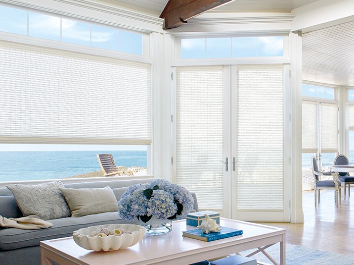 Tall windows and French door overlooking the ocean with white furinture and light blue hydrangeas on coffee table in front of light blue couch